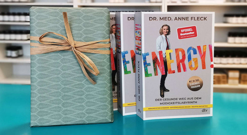 Bücher „ENERGY!“ von Dr. med. Anne Fleck im Regal neben einem Geschenkpaket – SPIEGEL-Bestseller zur Selbsthilfe bei Müdigkeit, mit 30-Tage-Programm zur Stärkung des Immunsystems und zur Entzündungsregulation.